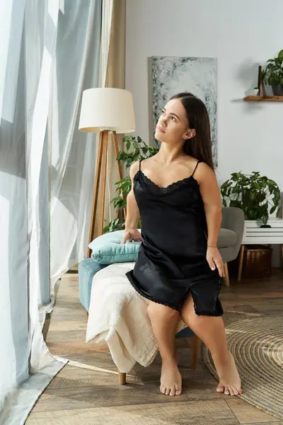 Une petite femme brune de petite taille s'assoit confortablement à la maison, regardant doucement par la fenêtre tout en appréciant son environnement. — Photo de stock