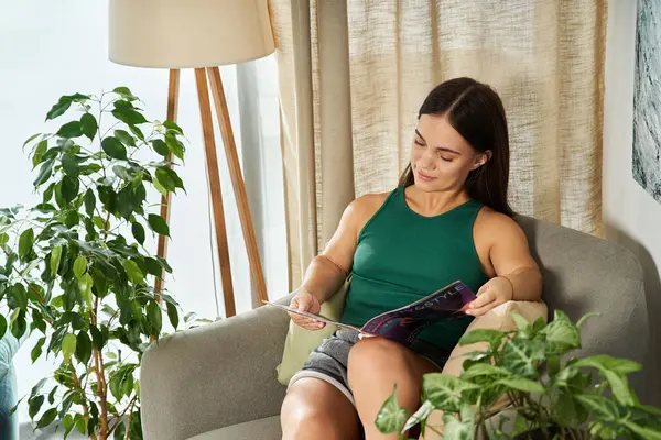 A petite brunette enjoys a peaceful moment at home, absorbed in a magazine while surrounded by vibrant plants. — Stock Photo