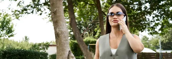 Une jeune femme brune avec une tenue élégante est à l'extérieur, bavardant joyeusement sur son téléphone, embrassant la beauté de la journée. — Photo de stock