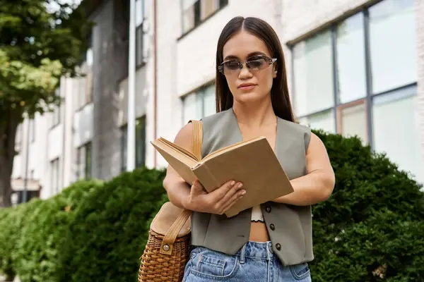 A short-statured brunette woman relaxes outdoors, absorbed in her book amidst lush greenery and urban vibes. — Stock Photo