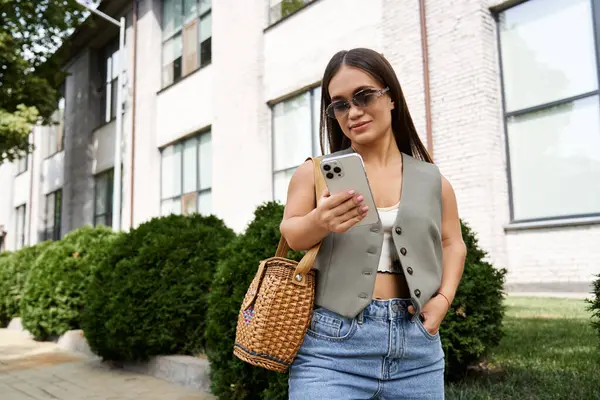 A young brunette woman with a cheerful demeanor explores her surroundings, attentively using her phone outside in the city. — Stock Photo