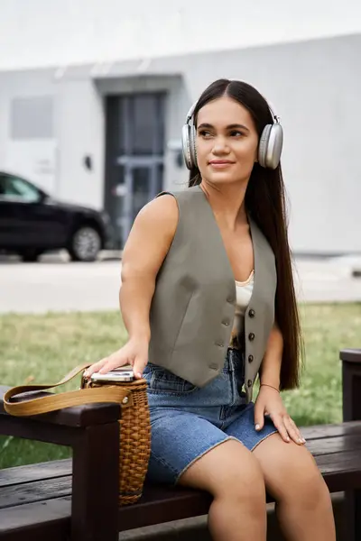 A young brunette woman with short stature relaxes outside, wearing headphones and a chic outfit while she enjoys some leisure time. — Stock Photo