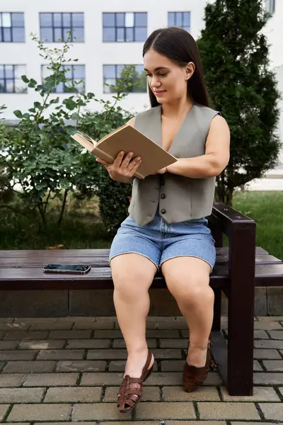 Eine junge brünette Frau mit einem charmanten Lächeln ist in ein Buch vertieft und genießt einen ruhigen Moment im Freien, umgeben von viel Grün. — Stockfoto