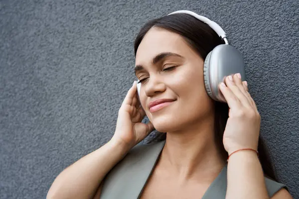 A short-statured brunette woman closes her eyes in bliss, immersed in music while outdoors on a bright day. — Stock Photo