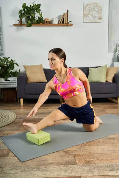 A determined young brunette stretches gracefully on a yoga mat at home, enhancing her flexibility and strength. — Stock Photo