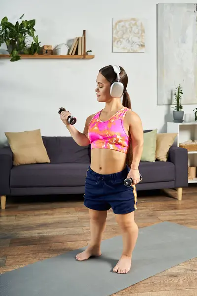 Eine entschlossene brünette Frau mit einer kurzen Statur macht zu Hause ein rigoroses Workout, hebt Hanteln und konzentriert sich auf ihre Fitnessreise. — Stockfoto