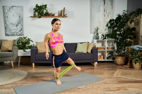 A brunette young woman with a short stature focuses on her workout at home, using resistance bands in her stylish living room. — Stock Photo