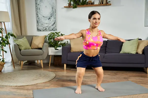 The young woman with a short stature enjoys a workout session in her cozy living room, focusing on her fitness and well-being. — Stock Photo