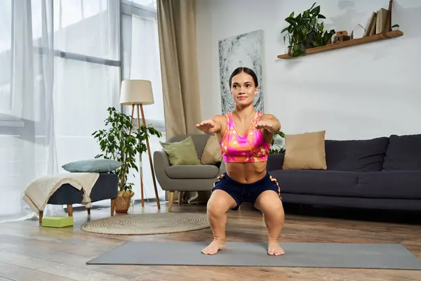Una joven morena decidida con una estatura corta realiza sentadillas en casa, mostrando su compromiso con el fitness y la salud. — Stock Photo