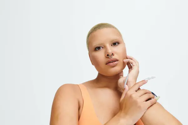 A confident young bald woman poses gracefully in vibrant attire against a plain background. — Stock Photo