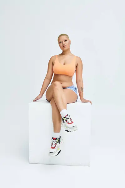 A confident young woman showcases vibrant fashion while seated on a geometric pedestal. — Stock Photo