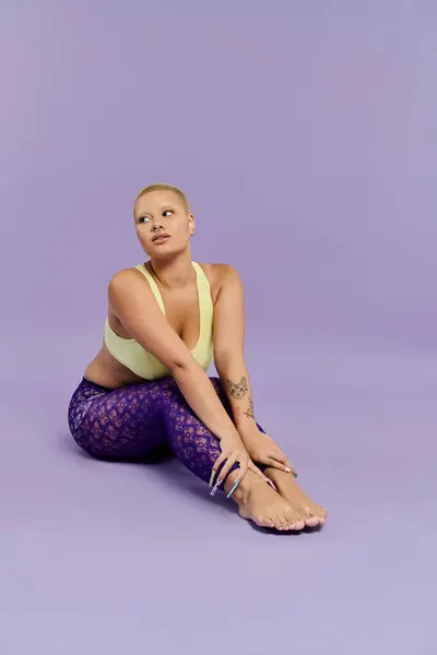 A young bald woman dressed in vivid colors leans and stretches elegantly on a pastel backdrop. — Stock Photo