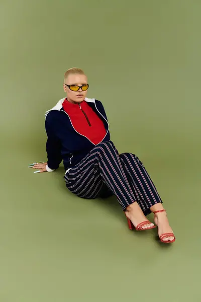 A young bald woman showcases her vibrant outfit while sitting stylishly on a green backdrop. — Stock Photo