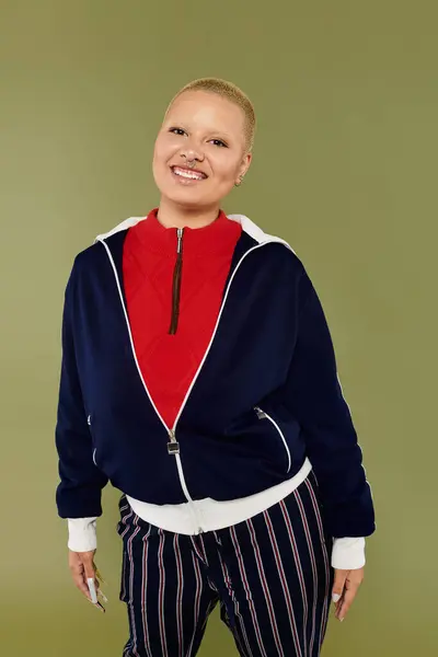 A cheerful young bald woman showcases her vibrant outfit while standing confidently. — Stock Photo