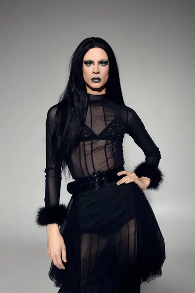 Una drag queen confiada exhibe un impresionante conjunto negro, de pie sobre un fondo gris. — Stock Photo