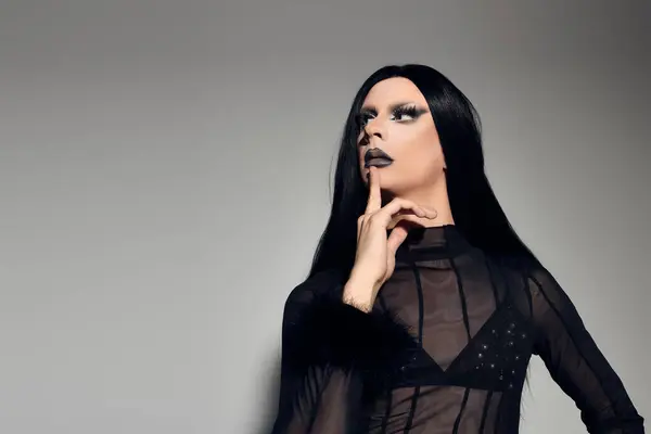 Une drag queen à la mode respire la confiance dans une tenue noire élégante, frappant une pose dans un cadre de studio. — Photo de stock