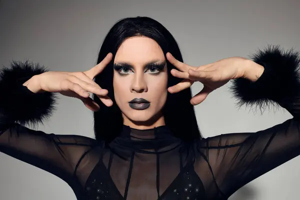 A fashionable drag queen showcases a stunning black outfit against a sleek grey backdrop, exuding confidence. — Stock Photo