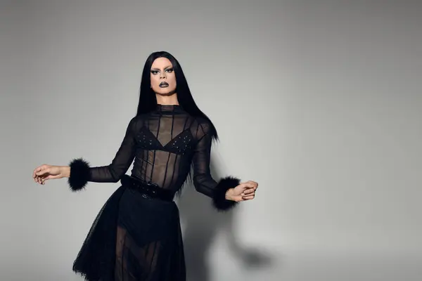 A confident gender fluid person embodies glamour in a chic black outfit against a grey background. — Stock Photo