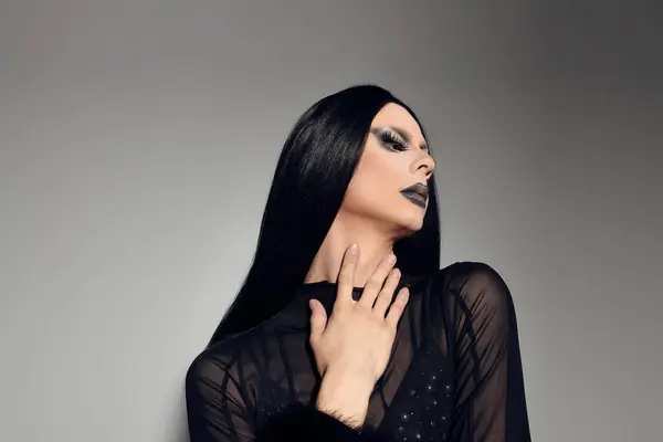 Dramatic lighting highlights a fashionable drag queen in a sleek black ensemble, showcasing bold expression. — Stock Photo