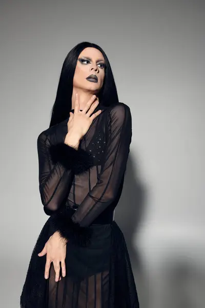 A fashionable drag queen showcases a stunning black outfit against a soft grey backdrop, exuding confidence. — Stock Photo