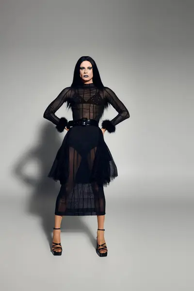A striking figure showcases a fashionable black outfit, exuding confidence against a minimalist grey backdrop. — Stock Photo