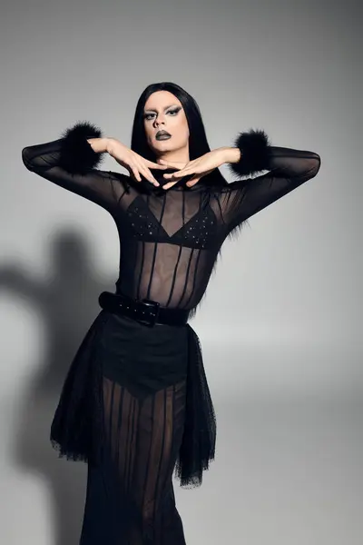 A fashionable drag queen showcases a black outfit with flair, exuding confidence against a grey backdrop. — Stock Photo