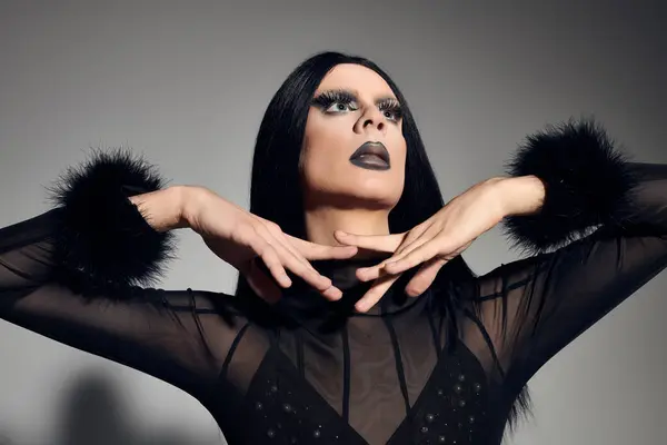 A fashionable gender fluid individual showcases a stunning black outfit with dramatic makeup against a grey backdrop. — Stock Photo