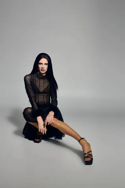 A stylish drag queen poses in a sleek black outfit against a minimalist grey backdrop, radiating confidence. — Stock Photo