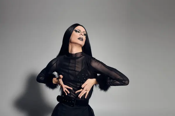 A fashionable drag queen confidently poses in a sleek black outfit against a minimalist grey backdrop. — Stock Photo