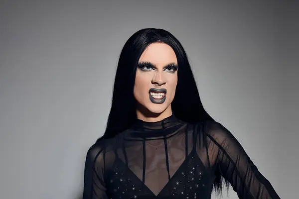 La drag queen alla moda posa fiduciosa in un elegante ensemble nero su uno sfondo neutro, trasudando arte. — Stock Photo