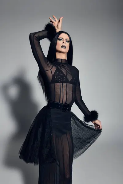 A confident gender fluid performer showcases their bold black attire against a sleek grey backdrop. — Stock Photo