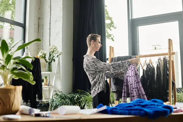 A gender fluid fashion designer selects vibrant fabrics in a bright studio space filled with lush plants. — Stock Photo