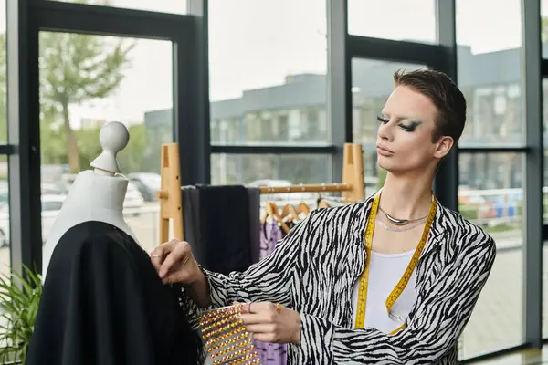 Un designer transgenre à la mode conçoit méticuleusement des vêtements uniques dans un studio lumineux. — Photo de stock