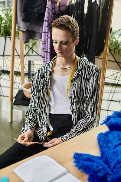 A gender fluid fashion designer focuses intently on their work amid a lively, colorful studio atmosphere. — Stock Photo