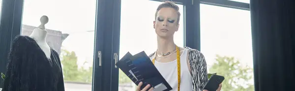 In a bright studio, a fashionable transgender designer reviews design sketches and fabric swatches with flair. — Stock Photo