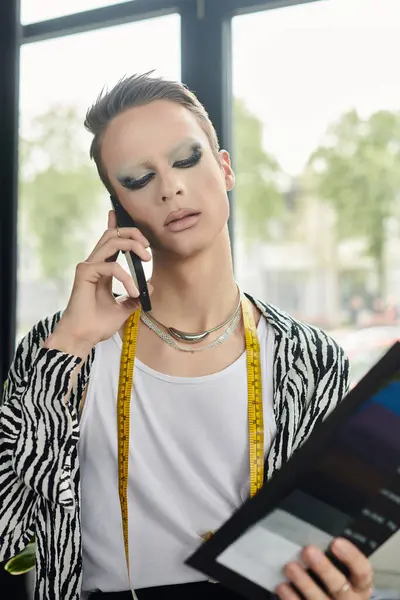 Um estilista transgênero na moda discute ideias no telefone enquanto mostra as escolhas de tecido. — Fotografia de Stock