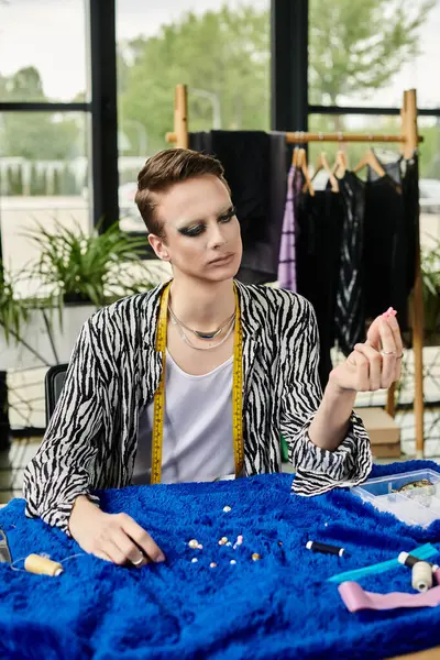 A stylish gender fluid designer examines fabric details at a bright studio workspace filled with inspiration. — Stock Photo