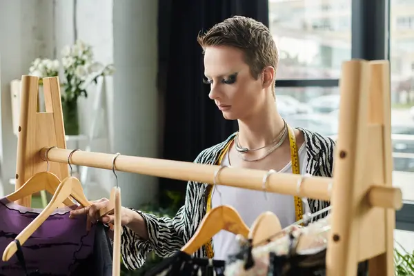 In a vibrant studio, a gender fluid designer carefully selects garments, showcasing unique fashion creativity. — Stock Photo