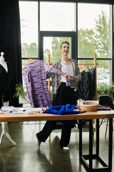 A stylish transgender fashion designer joyfully presents unique designs in a bright studio workspace. — Stock Photo