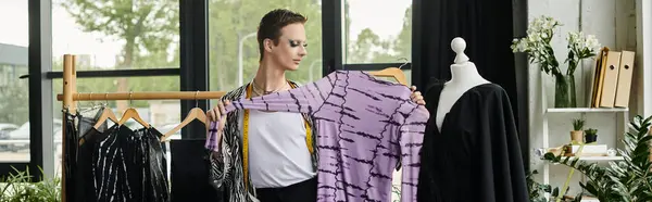 A fashionable gender fluid designer holds up a striking garment, immersed in creativity in their studio. — Stock Photo