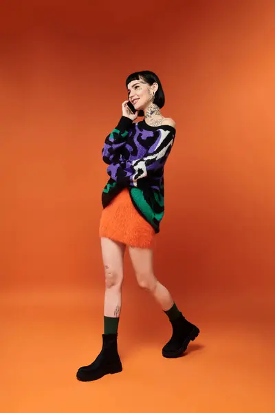 A young woman with short hair and tattoos joyfully poses in a bright sweater, showcasing her style in a studio. — Stock Photo