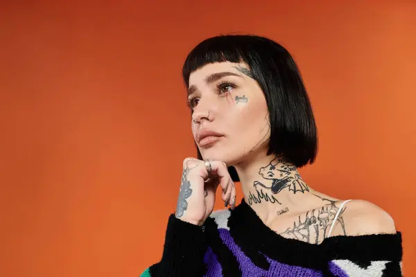 Una joven con tatuajes atrevidos posa en un suéter colorido, irradiando confianza e individualidad. - foto de stock