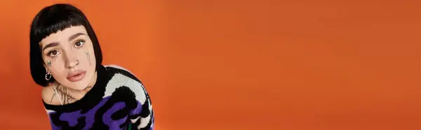 A confident young woman showcases her style in a bright sweater, accentuated by bold tattoos and a warm background. — Stock Photo