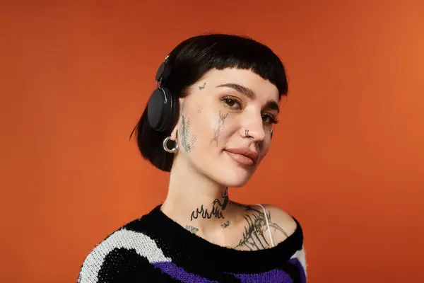Une jeune femme aux cheveux courts ornée de tatouages met en valeur son style dans un pull lumineux, rayonnant de confiance. — Photo de stock
