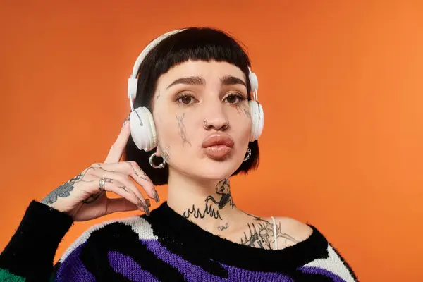 A young woman with short hair and vivid tattoos expresses attitude while wearing a colorful sweater. — Stock Photo