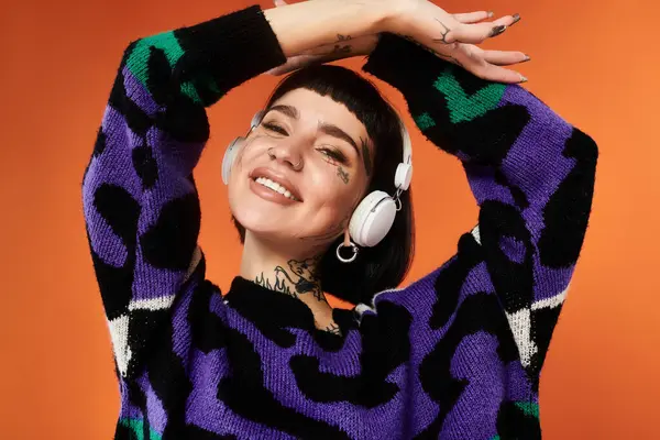 A young woman with short hair and tattoos radiates happiness while posing in a colorful sweater, smiling brightly. — Stock Photo