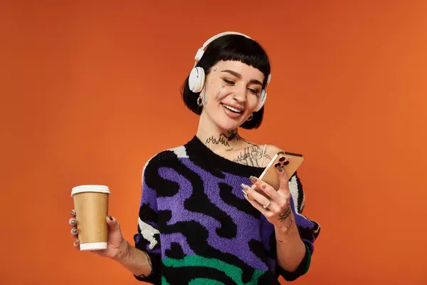 A youthful woman with a stylish look smiles while listening to her music, holding a coffee cup. — Stock Photo