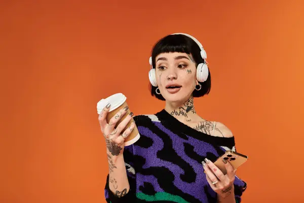 This young woman, adorned with tattoos, joyfully sips coffee while listening to music in a lively studio. — Stock Photo