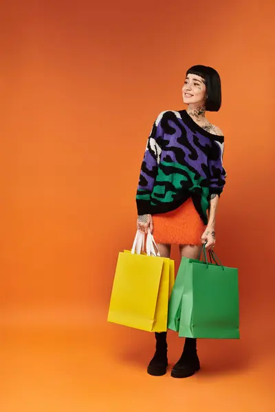 Una mujer joven con estilo muestra sus tatuajes audaces mientras sostiene bolsas de compras brillantes en un entorno alegre. - foto de stock