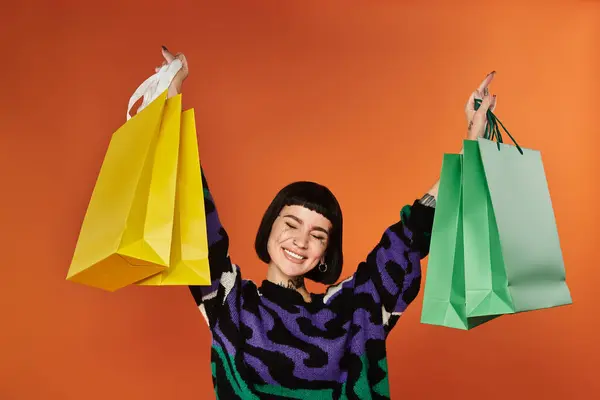 Una giovane donna con i capelli corti alla moda celebra mentre tiene vivaci borse della spesa in un ambiente da studio. — Foto stock